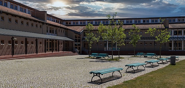 Schulhof mit Schulgebäude und Bänken und Wolken